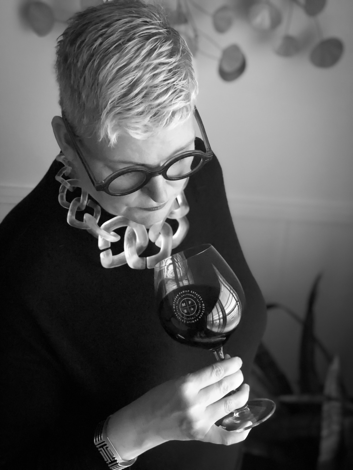 Lynda Barnes looking into a glass of wine with the Metzker Family Estate logo on the side.